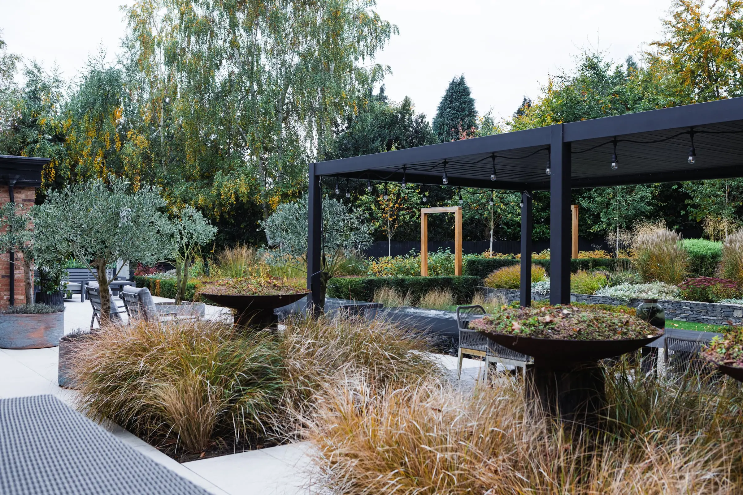Naturalistic grasses and sculptural bowl planters beneath a contemporary pergola in Woburn Sands